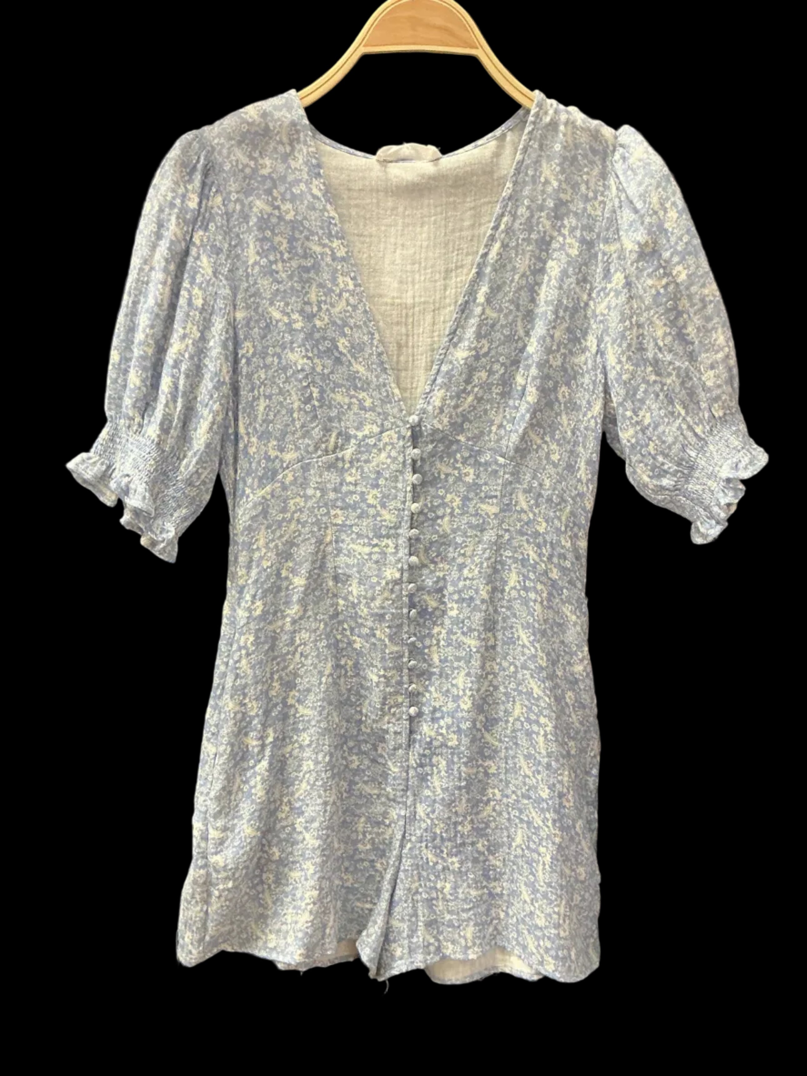 A light blue and white textured knit top with ruffled sleeves.
laid flat on a black fabric background and hanging from a wooden hanger.